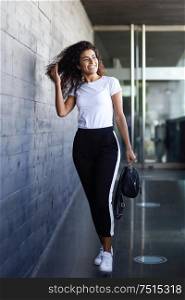Young African woman with black curly hairstyle walking near business building. Happy Arab girl in sport clothes in the street.. Young African woman with black curly hairstyle walking near business building