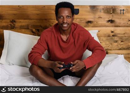 Young afro american man having fun playing games in the bed.