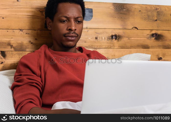 Young afro american man using his laptop in bed.