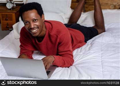 Young afro american man using his laptop in bed.