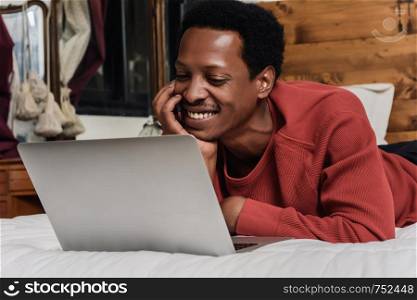 Young afro american man using his laptop in bed.