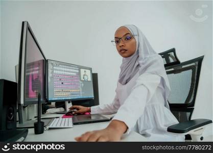 Young Afro-American modern Muslim businesswoman wearing a scarf in a creative bright office workplace with a big screen. High-quality photo. Young Afro-American modern Muslim businesswoman wearing a scarf in a creative bright office workplace with a big screen.
