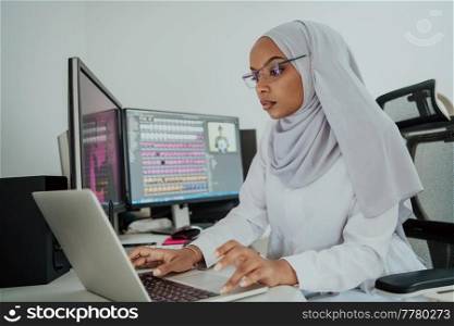 Young Afro-American modern Muslim businesswoman wearing a scarf in a creative bright office workplace with a big screen. High-quality photo. Young Afro-American modern Muslim businesswoman wearing a scarf in a creative bright office workplace with a big screen.