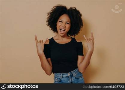 Young afro-american rock star, hands in rock sign, shouting with emotion, carefree, against beige background