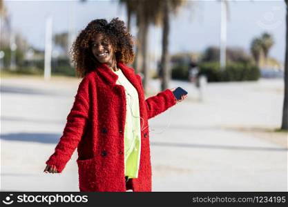 Young afro american woman laughing while dancing outdoors with red jacket