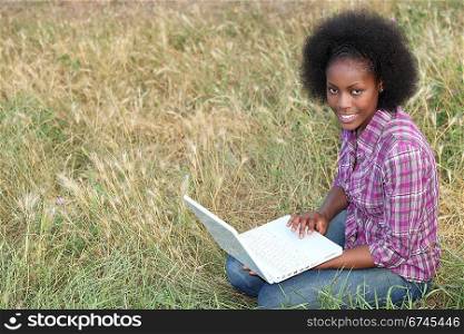 young Afro-American woman sitting on the grass with her laptop