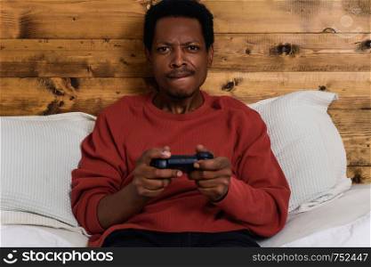 Young afro man having fun playing games in the bed.