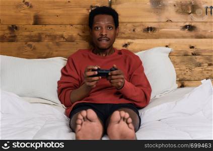 Young afro man having fun playing games in the bed at home