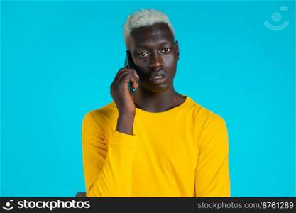 Young afro man speaks serious on phone. Guy holding and using smart phone. Blue studio background. Young afro man speaks serious on phone. Guy holding and using smart phone. Blue studio background.