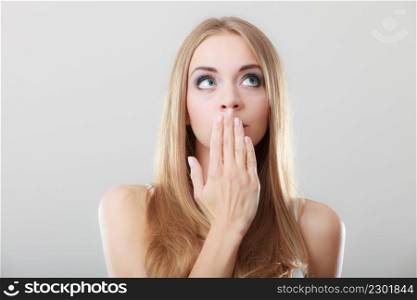 Young amazed woman covering her mouth with hand on gray