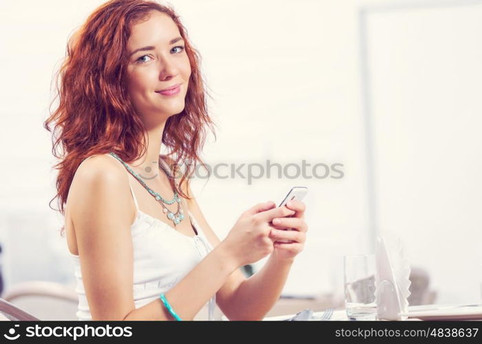 Young and attractive woman sitting in cafe and using cellphone. Texting massages at cafe