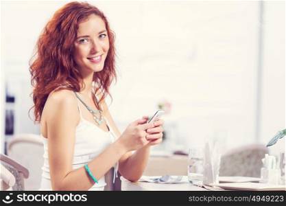 Young and attractive woman sitting in cafe and using cellphone. Texting massages at cafe