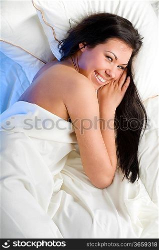 young and beautiful brunette in a bed looking in camera smiling
