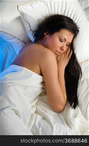 young and beautiful brunette in a bed sleeping between pillow