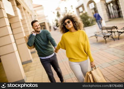 Young and cheerfull couple walking along street with shopping bags