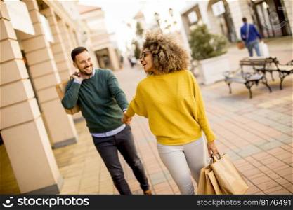 Young and cheerfull couple walking along street with shopping bags