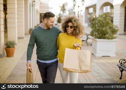 Young and cheerfull couple walking along street with shopping bags