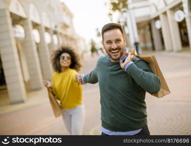 Young and cheerfull couple walking along street with shopping bags