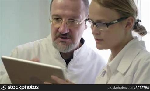 Young and experienced doctors in glasses discussing treatment issue using tablet computer. Man giving a full explanation to the woman
