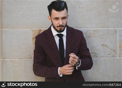 Young and fashionable man buttoning a cuff and posing outdoor on a stone wall background