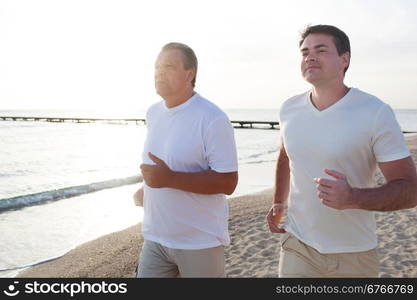 Young and mature man jogging in the beach. Evening sun shining brightly. Sport in vacation time