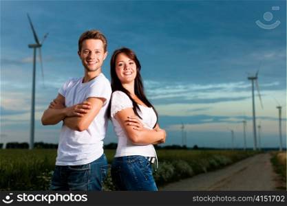 Young and powerful couple in front of energy windmill in the evening; a storm is coming