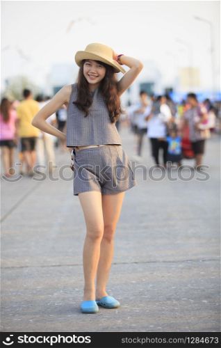 young and pretty asian woman wearing straw hat standing and posting with crowded behind