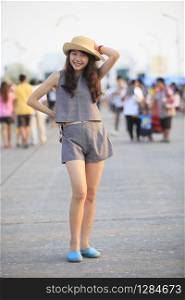 young and pretty asian woman wearing straw hat standing and posting with crowded behind
