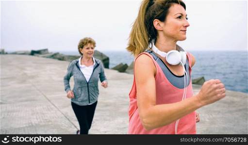 Young and senior sportswoman running by sea pier. Young and senior sportswoman running