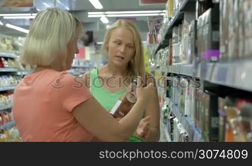 Young and senior woman shopping in the supermarket. Senior woman selecting tea, girl helps to make right choice