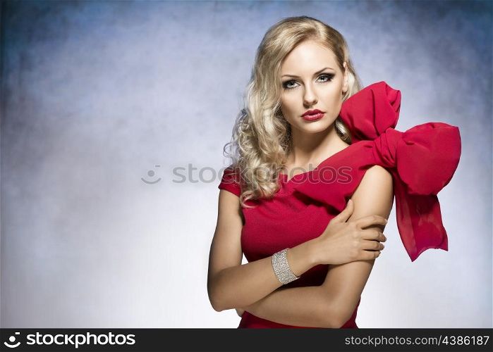 young and sexy beautiful blond woman in red dress with nice hair style and a big bow on shoulder.looking in camera&#xA;