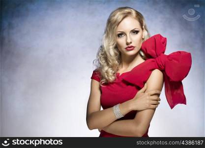 young and sexy beautiful blond woman in red dress with nice hair style and a big bow on shoulder.looking in camera&#xA;