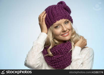 young and sexy blond girl wearing purple scarf and hat in winter dress on light blue background