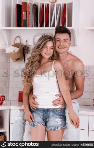 Young and sexy couple on the kitchen. Lovely beautiful couple standing and hugging on a kitchen at home. Both are looking at each other and smiling. Young and sexy couple on the kitchen. Lovely beautiful couple standing and hugging on a kitchen at home. Both are looking at each other and smiling.