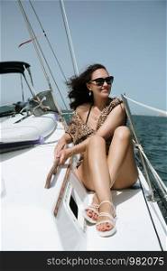 Young and sexy woman in tunic sitting on sailboat, enjoying summer vacation in sea cruise