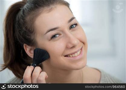 young and smiling woman applying a powder on her face