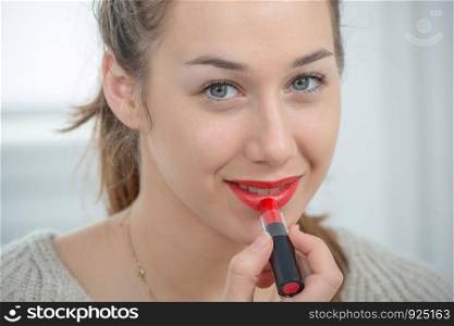 young and smiling woman putting a lipstick