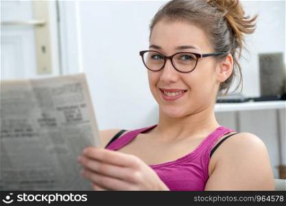 young and smiling woman with glasses, reading a newspaper