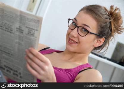young and smiling woman with glasses, reading a newspaper