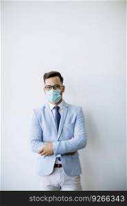 Young and stylish business man with protective face mask stands by the wall in the office