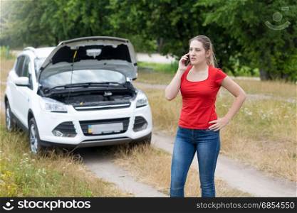 Young angry woman calling for help next to broken car