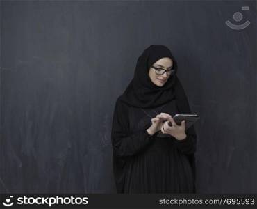 Young Arab businesswoman in traditional clothes or abaya with tablet computer in front of black chalkboard representing modern islam fashion technology