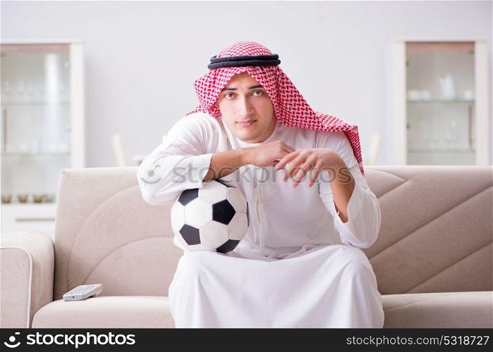 Young arab man watching football sitting on sofa