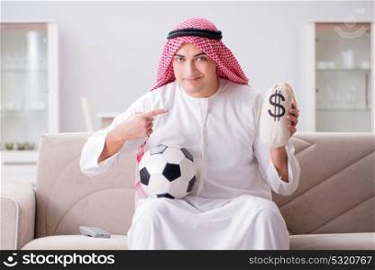 Young arab man watching football sitting on sofa