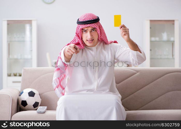 Young arab man watching football sitting on sofa