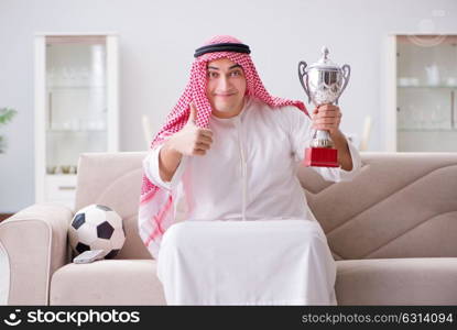 Young arab man watching football sitting on sofa