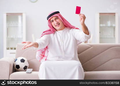 Young arab man watching football sitting on sofa