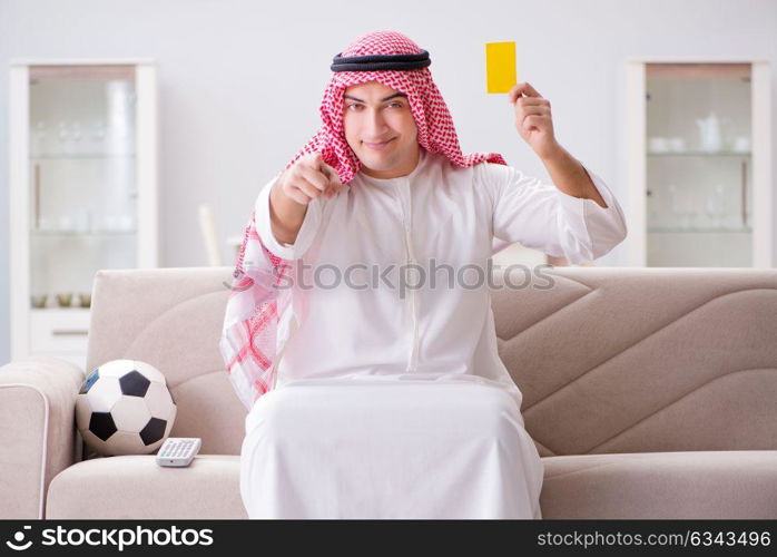 Young arab man watching football sitting on sofa