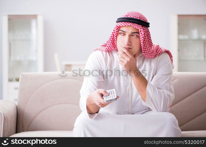 Young arab man watching tv sitting on the sofa