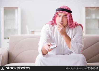 Young arab man watching tv sitting on the sofa